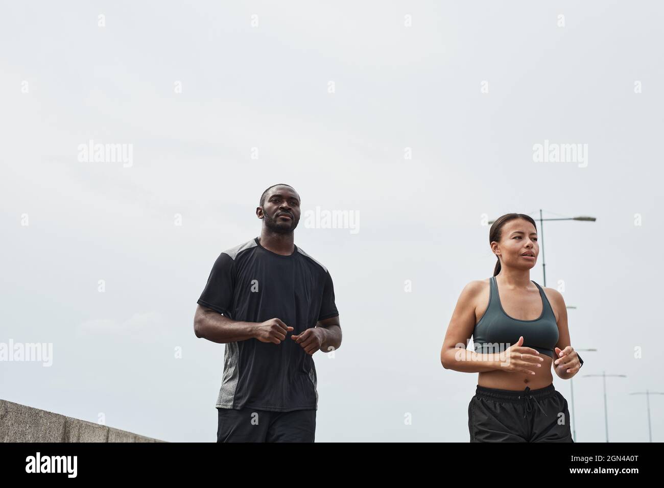 Pareja joven africana corriendo juntos por la mañana al aire libre contra el cielo azul Foto de stock
