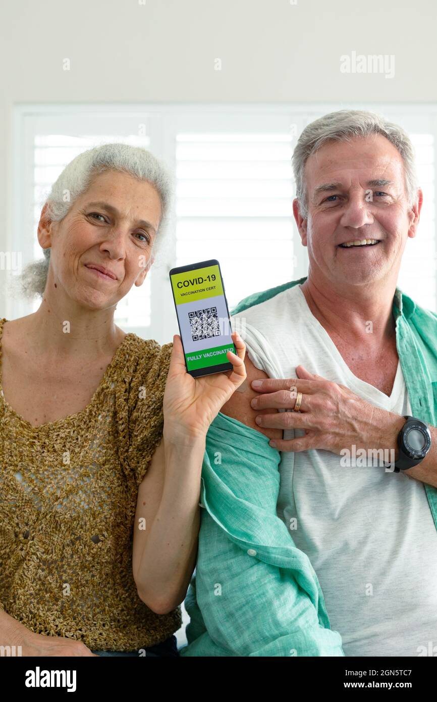 Sonriente pareja mayor caucásica mostrando teléfono inteligente con pasaporte de vacuna covid en la pantalla Foto de stock