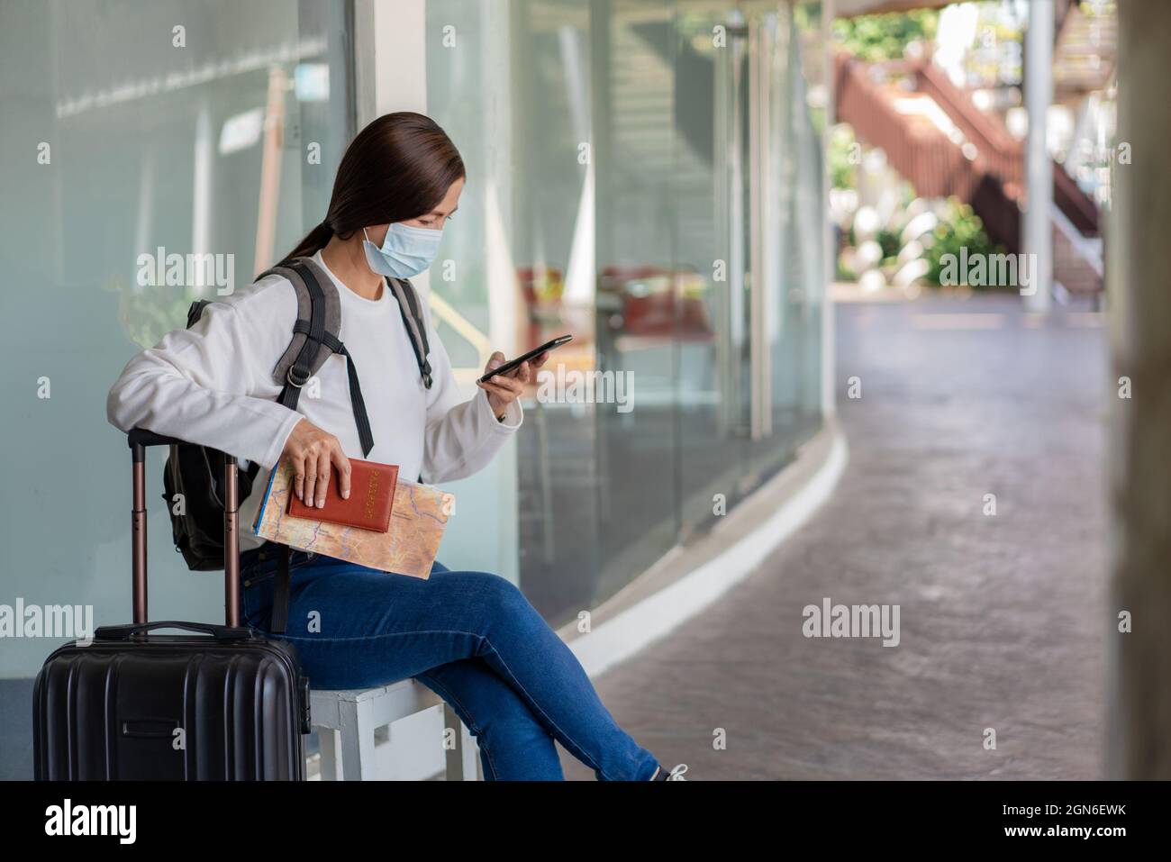Viajes. Una mujer en una camisa blanca de manga larga y jeans, con una  máscara. Siéntese en la silla y lea un mapa en su mano mientras la maleta y  la mochila