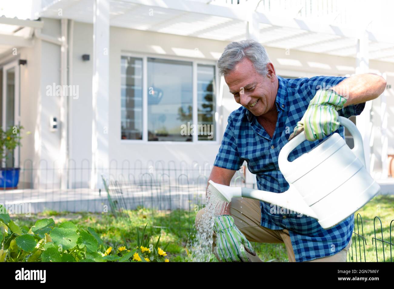 Tiempo De Jardinería. Sonriente Hombre De Cabello Oscuro Con Guantes  Protectores Agachado, Regando Spatifilium Con Regadera Fotos, retratos,  imágenes y fotografía de archivo libres de derecho. Image 147757909