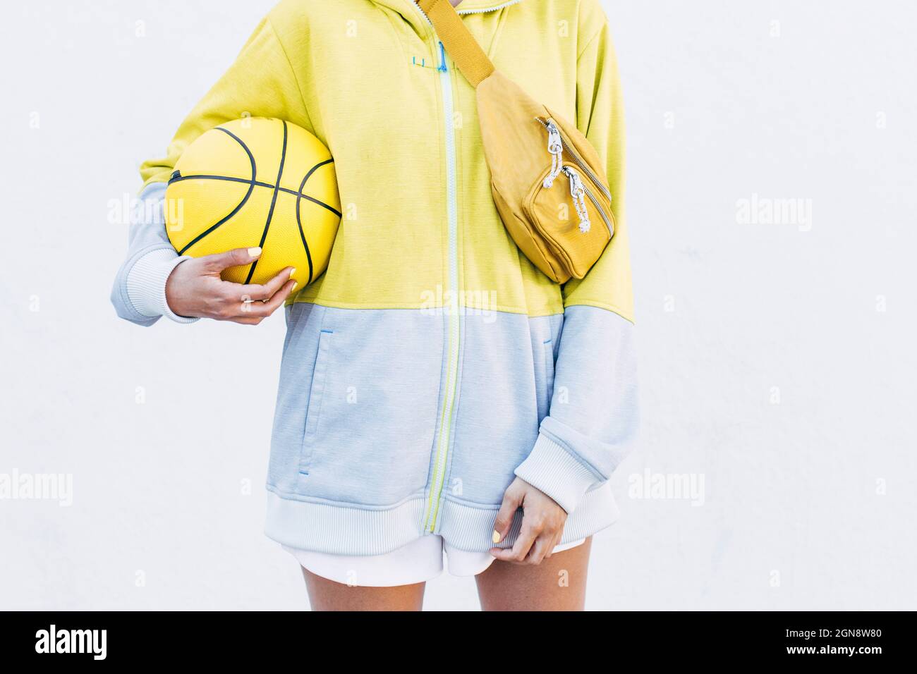 Joven jugador de baloncesto con pelota deportiva frente a la pared blanca Foto de stock