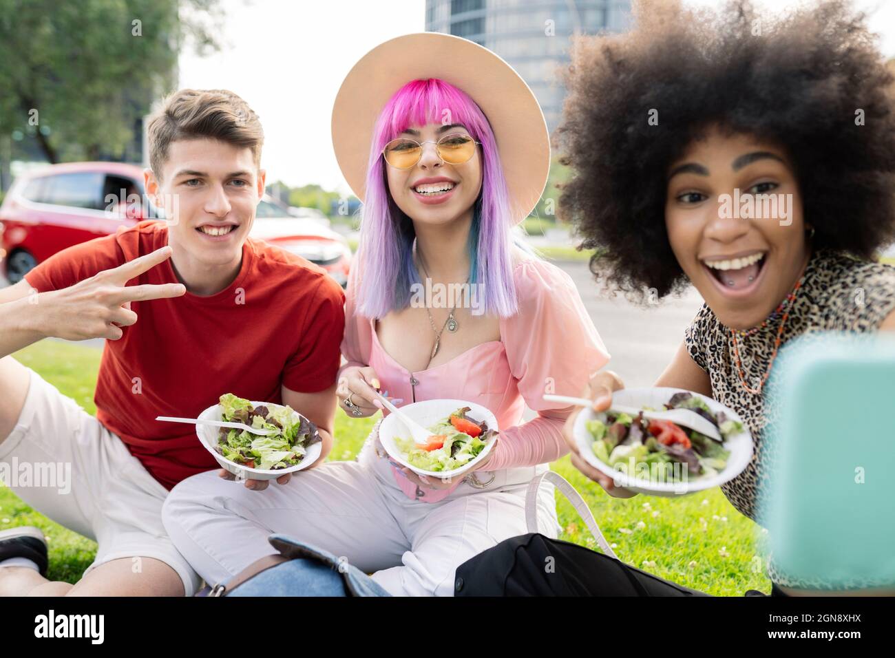 Alegre mujer tomando selfie con amigos mientras el hombre muestra señal de paz Foto de stock