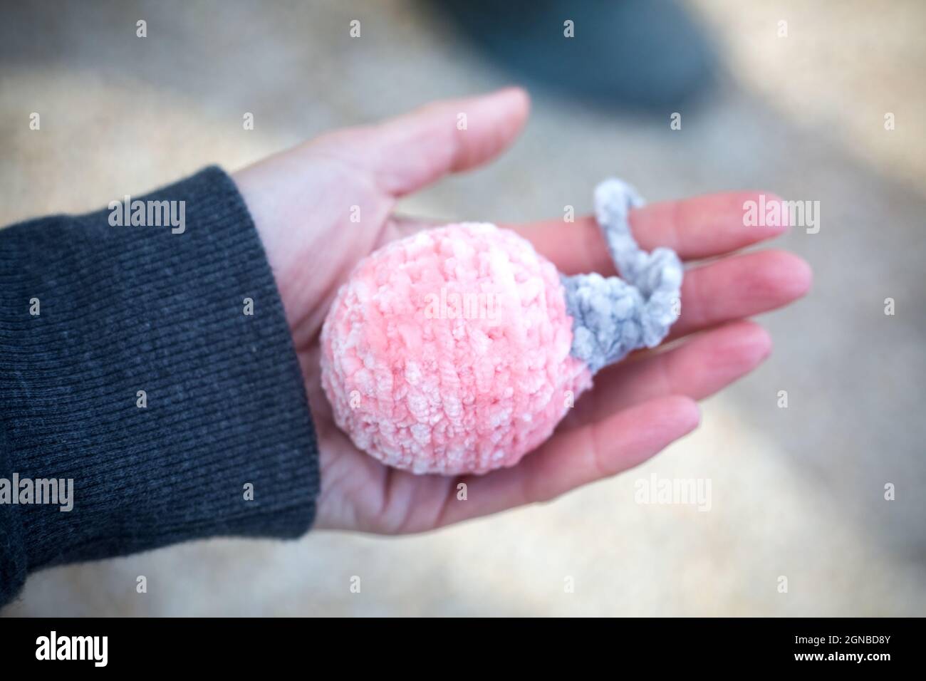 Rose año nuevo bola amigurumi en la mano de la mujer al aire libre. Tejido de peluche de hilo suave para la decoración navideña. Regalos navideños hechos a mano. Fabricación Foto de stock