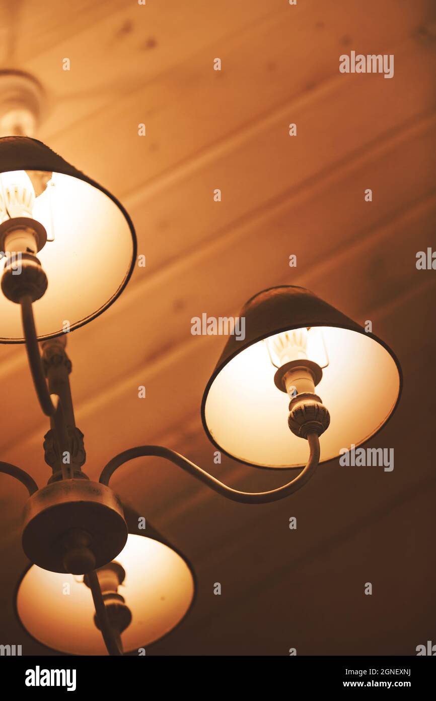 Las elegantes lámparas de estilo retro cuelgan en el fondo del techo de madera y emanan una cálida y acogedora luz por la noche. Hotel. Foto de stock