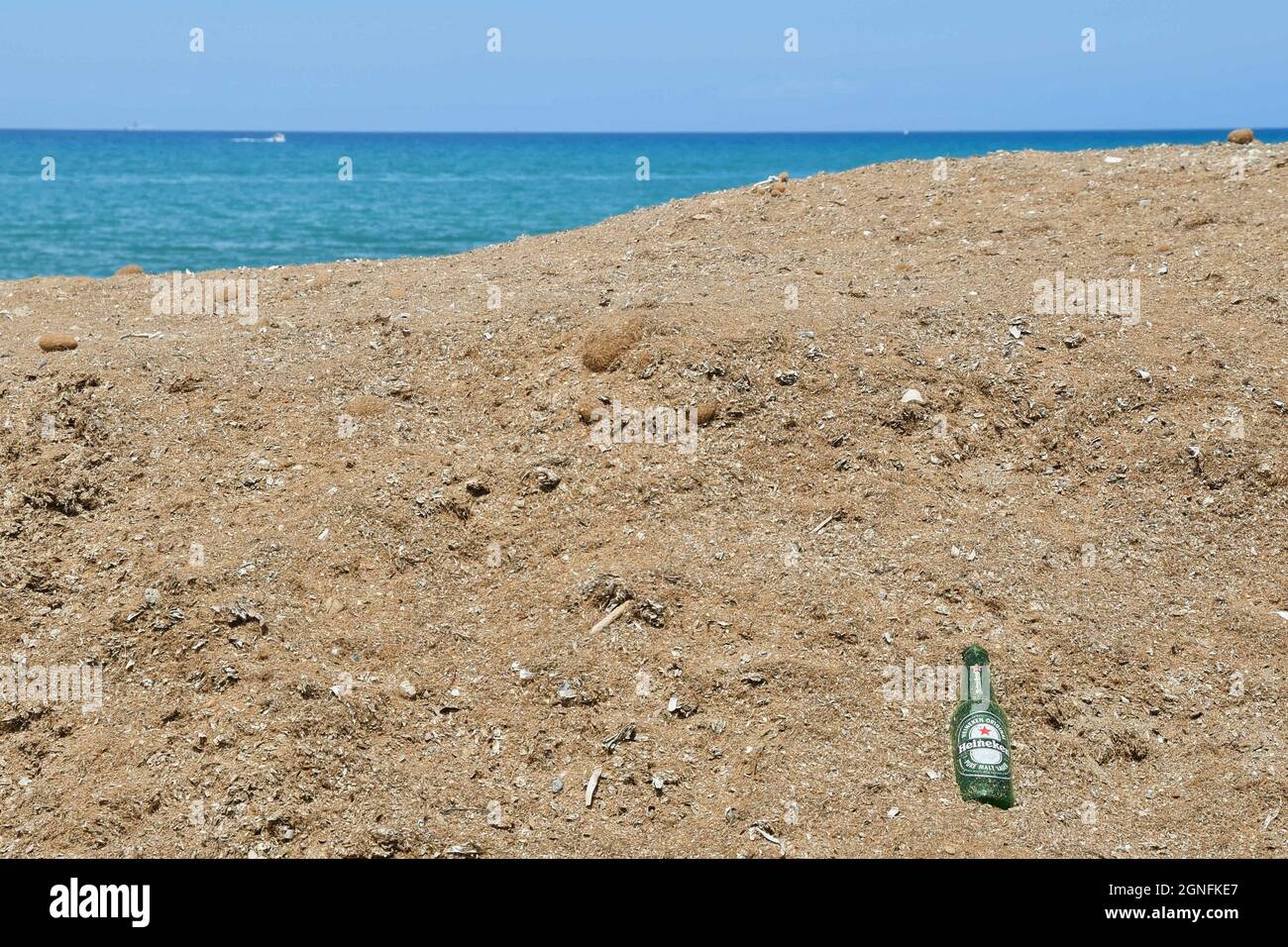 Una botella de cerveza vacía abandonada en la orilla arenosa con el mar en el fondo, concepto de la cuestión ambiental, San Vincenzo, Toscana, Italia Foto de stock