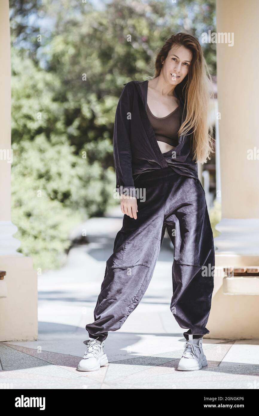 Una rubia de pelo largo en pantalones anchos y una camisa atada con un nudo  se encuentra entre las columnas en el parque en el día soleado Fotografía  de stock - Alamy