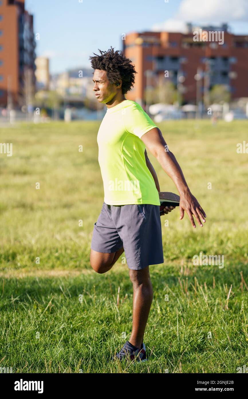 Hombre negro estirando sus cuadriceps después de correr al aire libre. Foto de stock