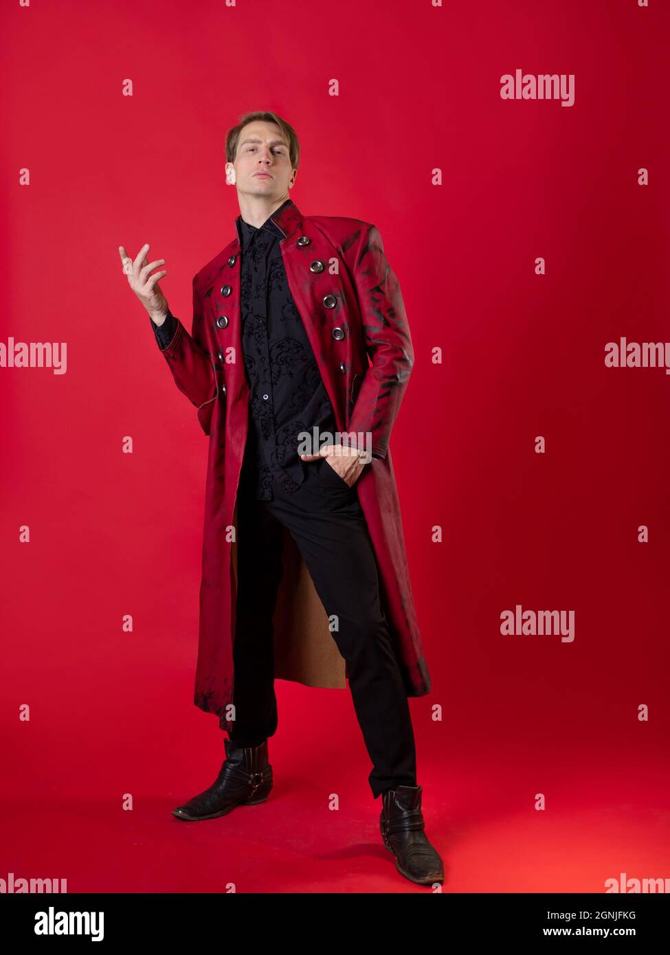 Un hombre joven extravagante con un atrevido abrigo rojo de estilo noir  vintage, con sus posturas épicas y un gesto de mano. Foto sobre fondo rojo  Fotografía de stock - Alamy