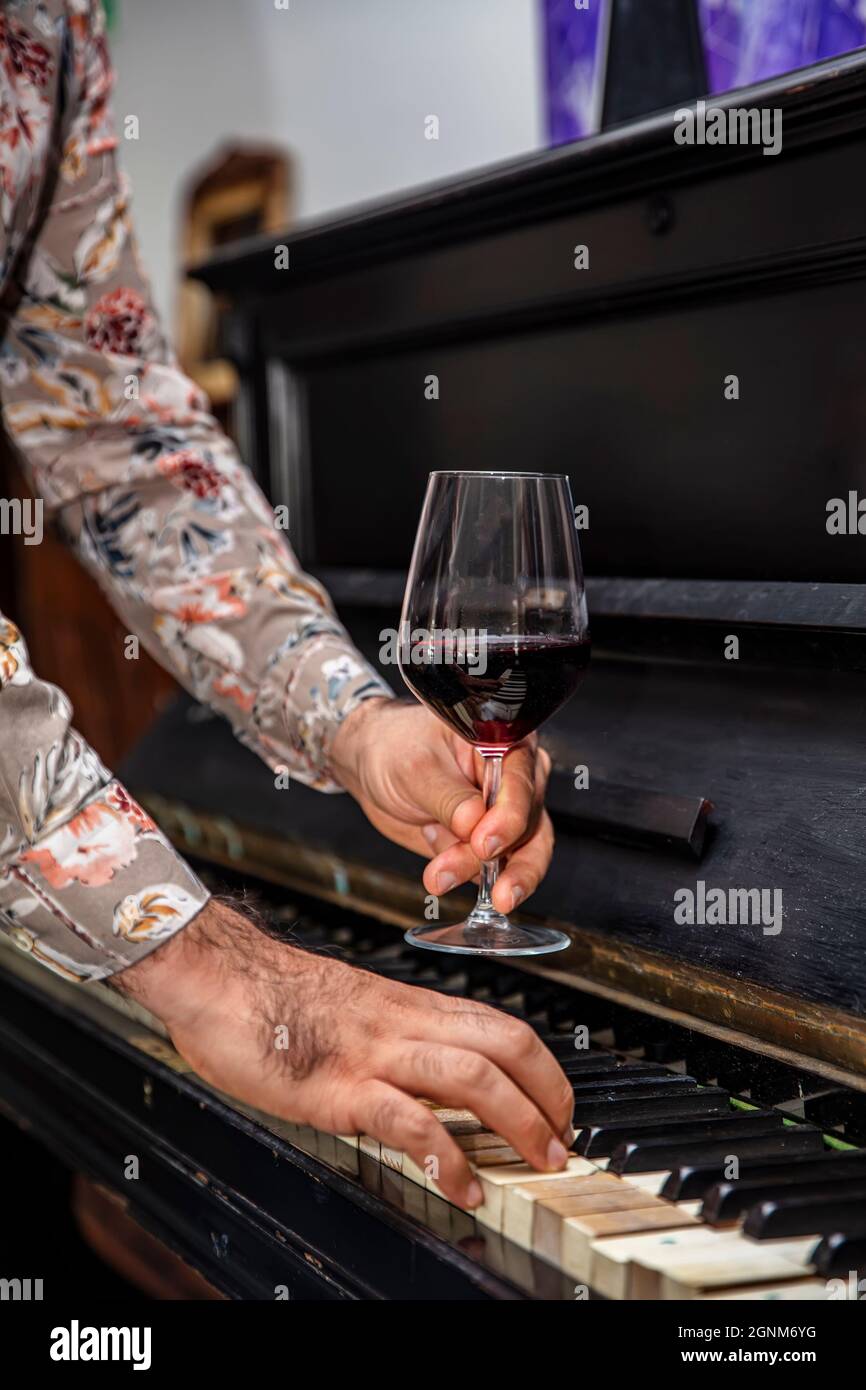 Antiguas llaves de piano clásicas y copa de vino. Una copa de vino tinto de  borgoña en una elegante copa de vino grabado que descansa sobre un teclado  de piano Fotografía de