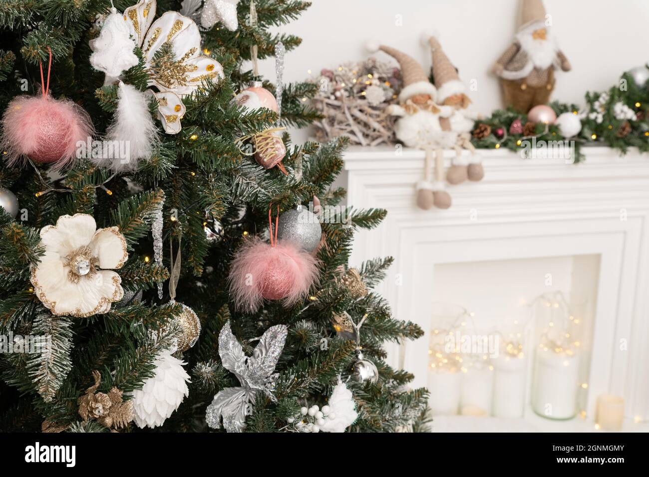 Árbol de Navidad decorado en colores rosa suave contra el fondo de la chimenea blanca clásica con decoraciones de Navidad. Detalles de las fiestas de Año Nuevo Foto de stock
