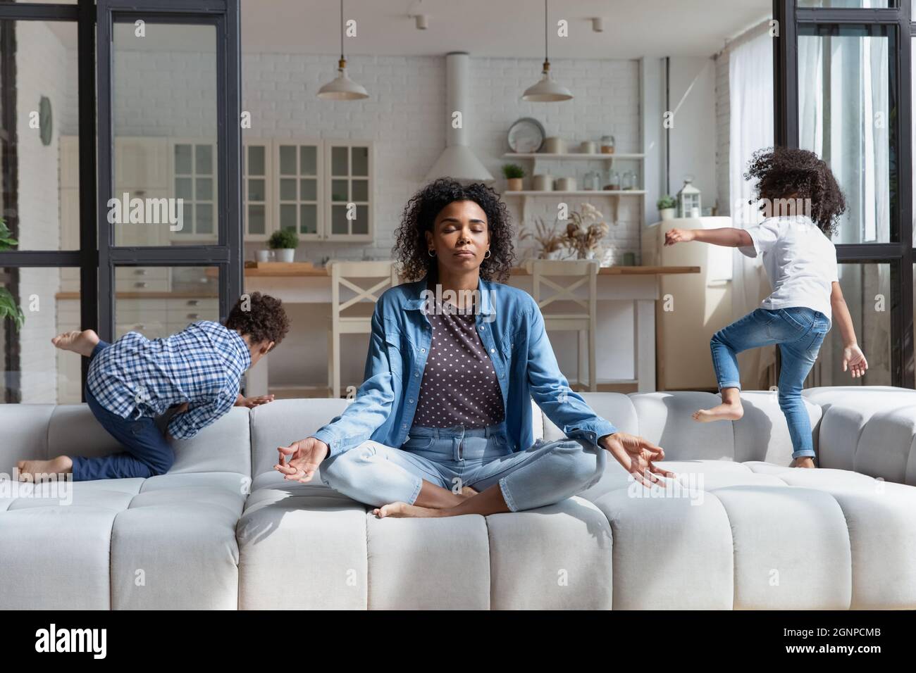 Mujer afroamericana meditando mientras los niños ruidosos saltan en el sofá Foto de stock