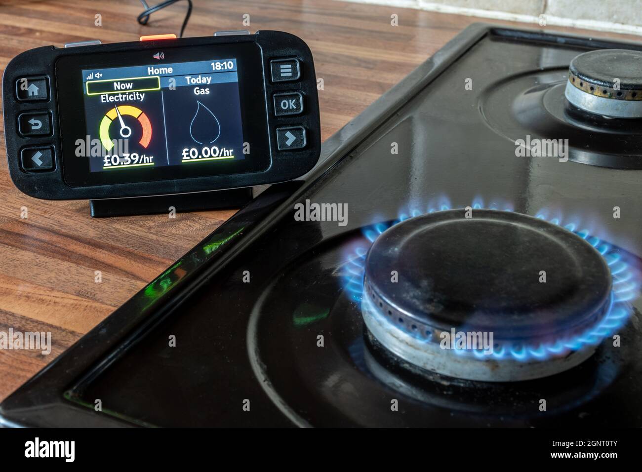 Mediciones inteligentes del uso de gas y electricidad en un monitor doméstico de energía inteligente junto a una cocina con llama de placa de gas Foto de stock
