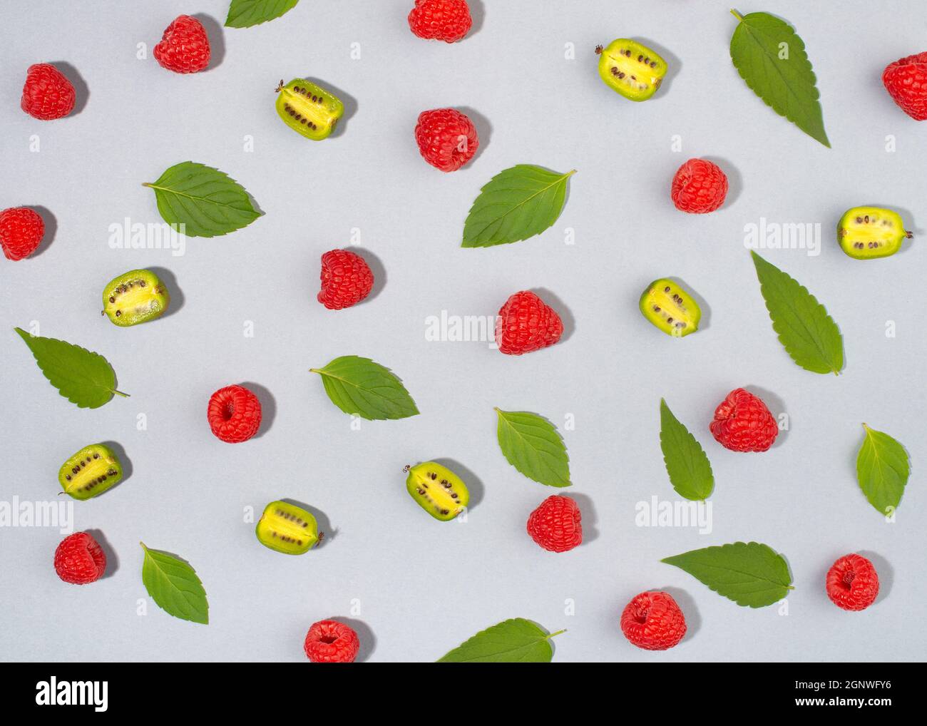 Fruto de actinidia arruta, frutos de kiwi, frambuesas y hojas de menta sobre fondo azul. Foto de stock