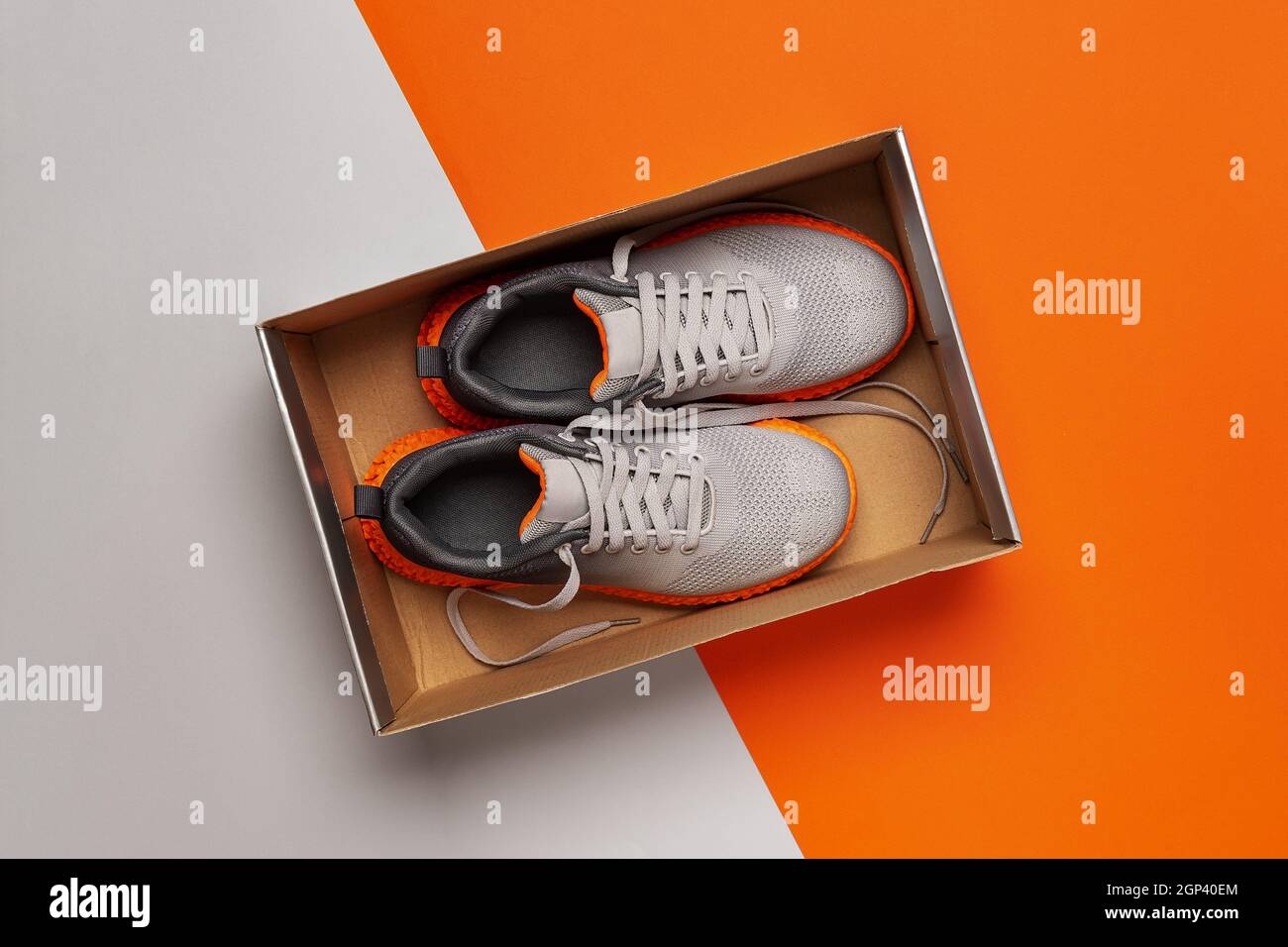 Nuevas sneakers de tela gris con suela naranja acanalada en la caja abierta  sobre fondo naranja gris. Zapatillas deportivas con tejido de malla con  estilo. Nueva caja de zapatos Fotografía de stock -