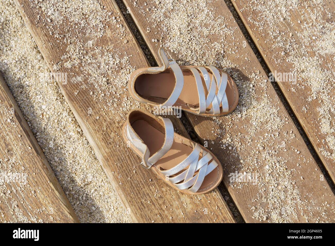 Sandalias de cuero plateado para niños sobre tabla de madera con arena en  días soleados Fotografía de stock - Alamy