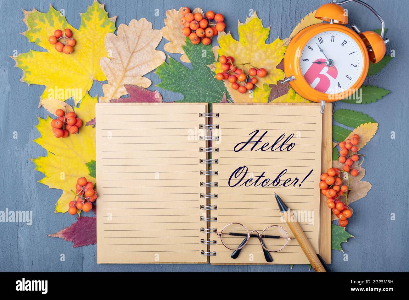 Reloj de alarma naranja, bloc de notas artesanal con las palabras HOLA  OCTUBRE, pluma y gafas sobre un fondo de otoño seco hojas de colores.  Planificación de día de trabajo CO Fotografía