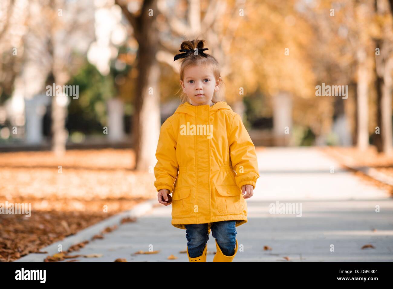 Bastante divertido niño niña de 2-3 años de edad usar chubasquero amarillo  brillante, botas de goma caminar en el parque sobre las hojas caídas al  aire libre. Temporada de otoño. Feliz niño