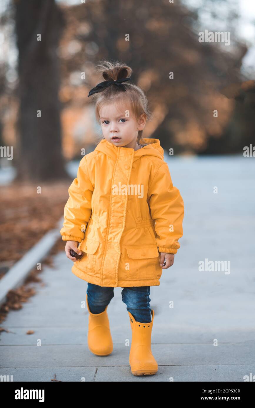 Bastante divertido niño niña de 2-3 años de edad usar chubasquero amarillo  brillante, botas de goma caminar en el parque sobre las hojas caídas al  aire libre. Temporada de otoño. Feliz niño