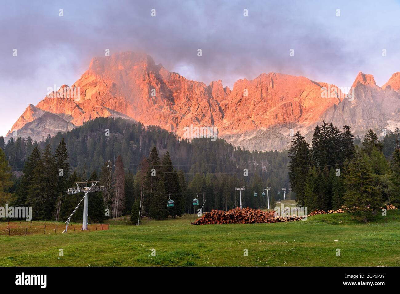 Pico rocoso en los Alpes Europeos cálidamente iluminado por un sol que se pone en una noche de otoño niebla. Los teleféricos que conducen a la montaña son visibles en primer plano Foto de stock