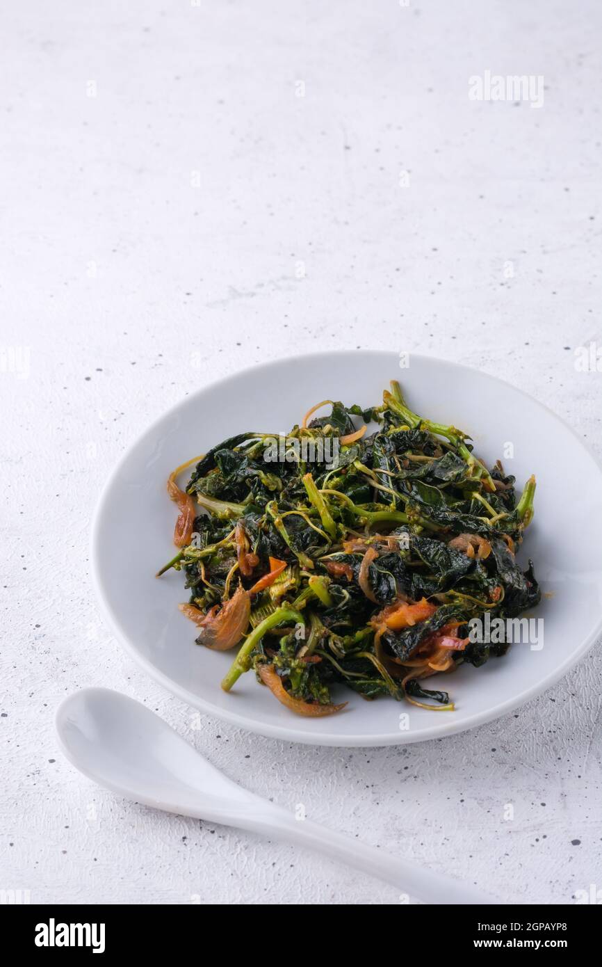amaranthus o plato de amaranto, plato de curry vegetariano de hoja verde sano con una cuchara sobre una superficie texturizada blanca Foto de stock
