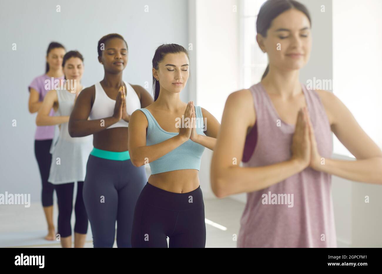 Grupo de mujeres jóvenes felices y relajadas haciendo el gesto Namaste durante la clase de yoga en el gimnasio Foto de stock