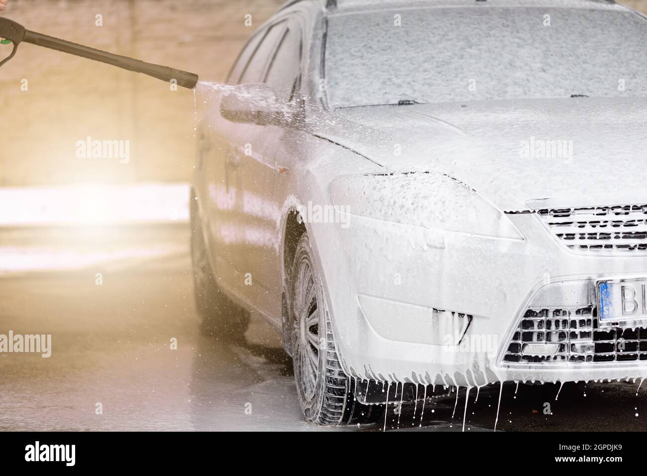 Limpieza de automóviles de alta presión con espuma en lavado de coches.  Lavar el coche usando una boquilla de agua y jabón. Vehículo purificando en  el lavabo de auto-servicio sobre el sol