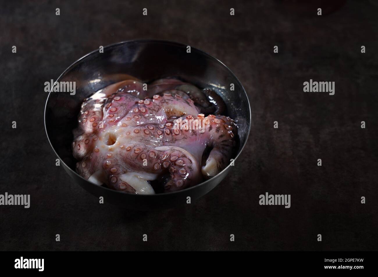 Un pulpo entero en un tazón de metal. Cocina pulpo. Fotos sin personas. Fondo oscuro. Platos de marisco. Alimentos de proteínas. Foto de stock