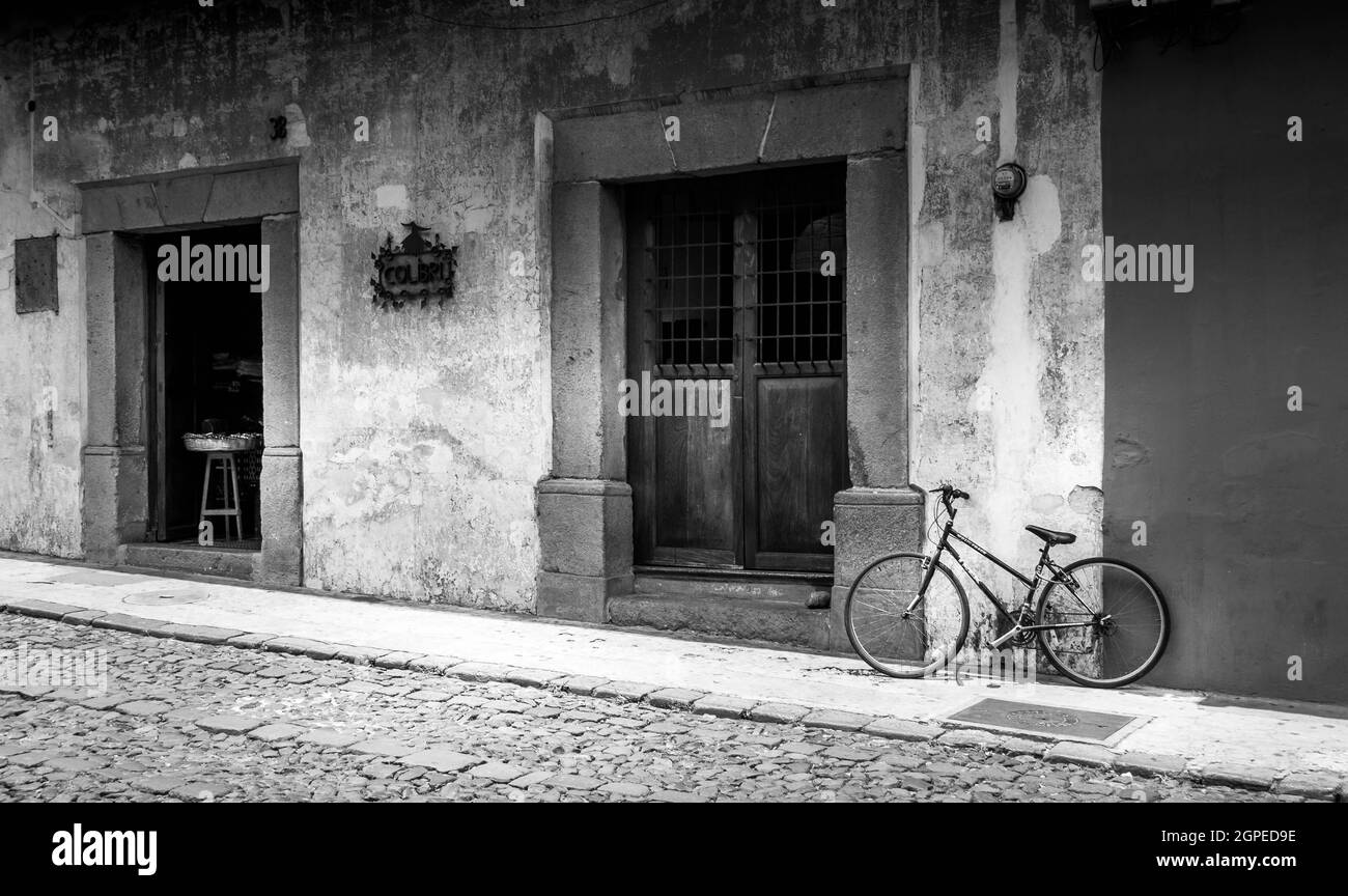 Imagen en blanco y negro de una bicicleta solitaria contra la pared fuera de un café en Cartagena, Colombia, Sudamérica. No hay gente. Foto de stock