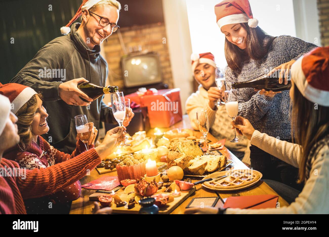 Grupo de amigos con sombreros de santa para celebrar la Navidad con champán y dulces de comida en casa - concepto de vacaciones de invierno con la gente disfrutando del tiempo Foto de stock