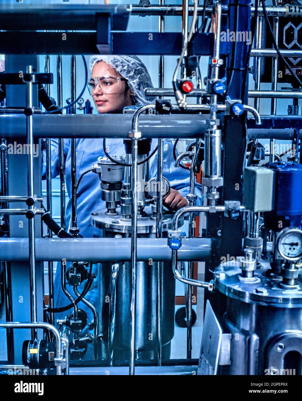 Mujer técnica que usa ropa limpia para ajustar el fermentador que cultiva las células de levadura que están genéticamente diseñadas para producir proteínas diseñadas f Foto de stock