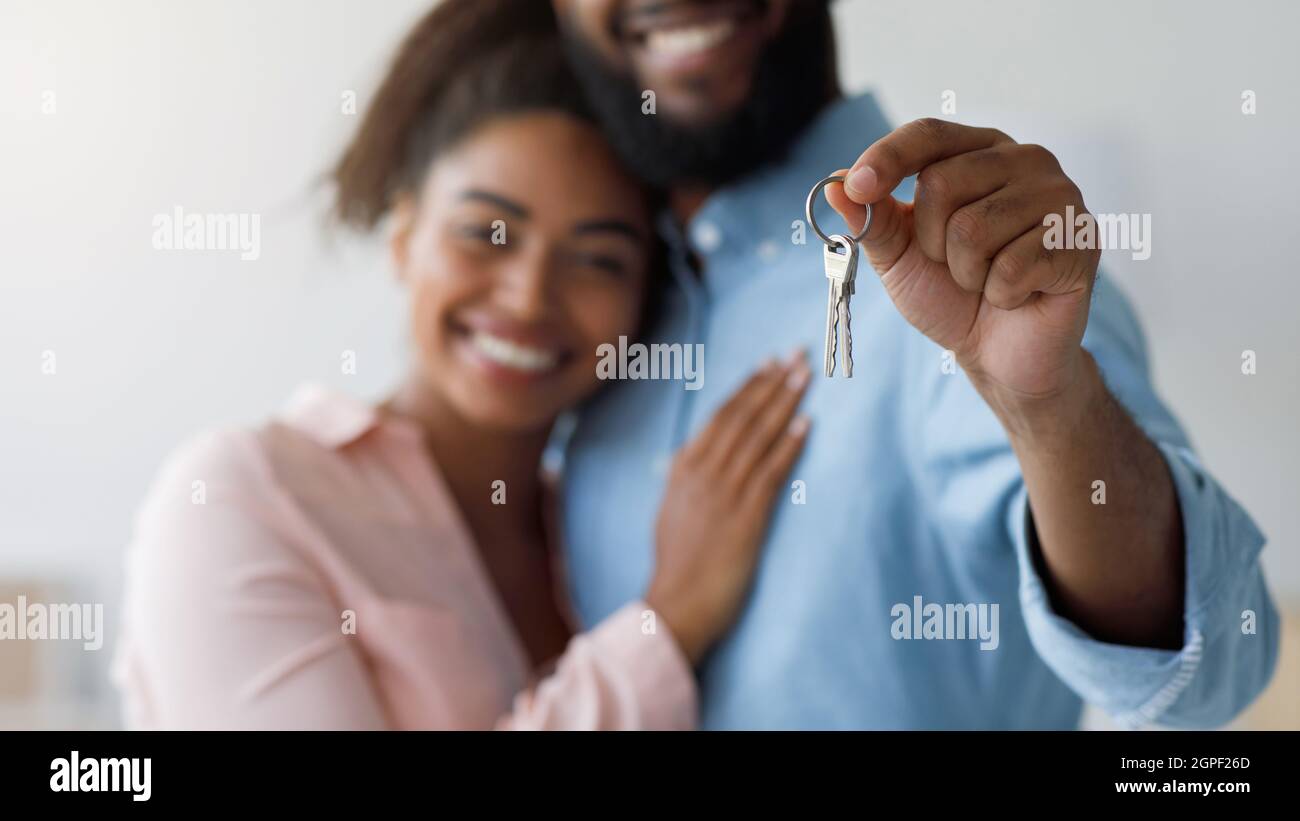 Satisfecho millennial negro pareja abrazando, mostrando las llaves de nuevo apartamento. Céntrese en las llaves de la primera casa Foto de stock
