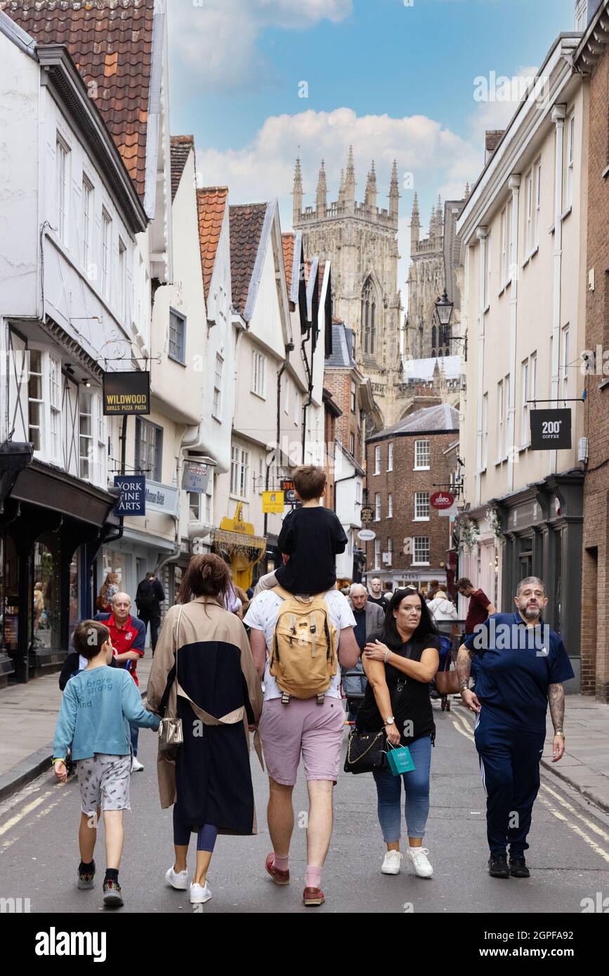 Escena de la calle York; gente incluyendo una familia con niños en vacaciones caminando por Low Petrgate hacia York Minster, centro de la ciudad de York, Reino Unido Foto de stock