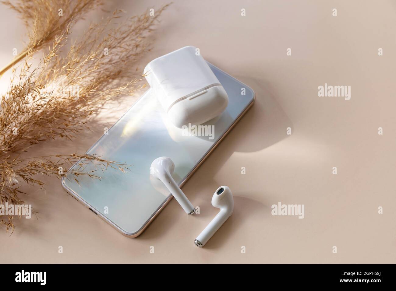 Minimal shot iPhone smartphone y de un par de auriculares inalámbricos  blancos, hierba seca sobre un fondo de colores pastel neutros. Tecnología  inalámbrica, mod Fotografía de stock - Alamy
