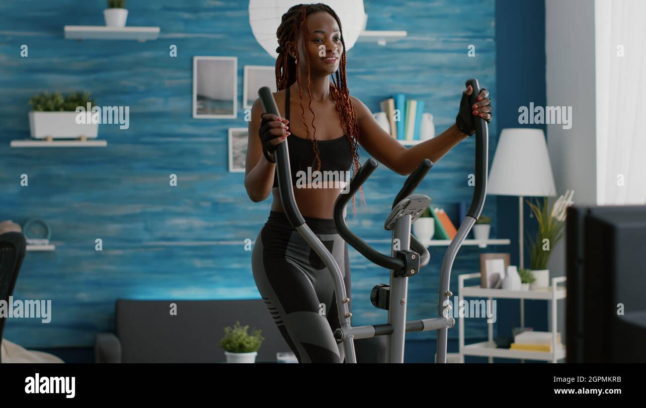 Mujer atlética negra haciendo entrenamiento cardiovascular en bicicleta  elíptica en la sala de estar durante la rutina de cardio por la mañana en  la sala de estar. Entrenador en deportes para calentar