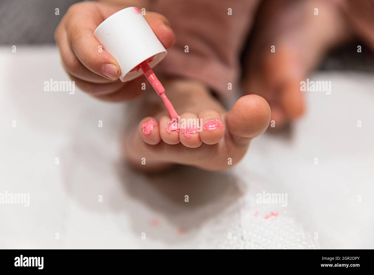 Uñas de los pies de la pintura infantil en rosa en la pedicura casera. Profundidad de campo superficial. Foto de stock