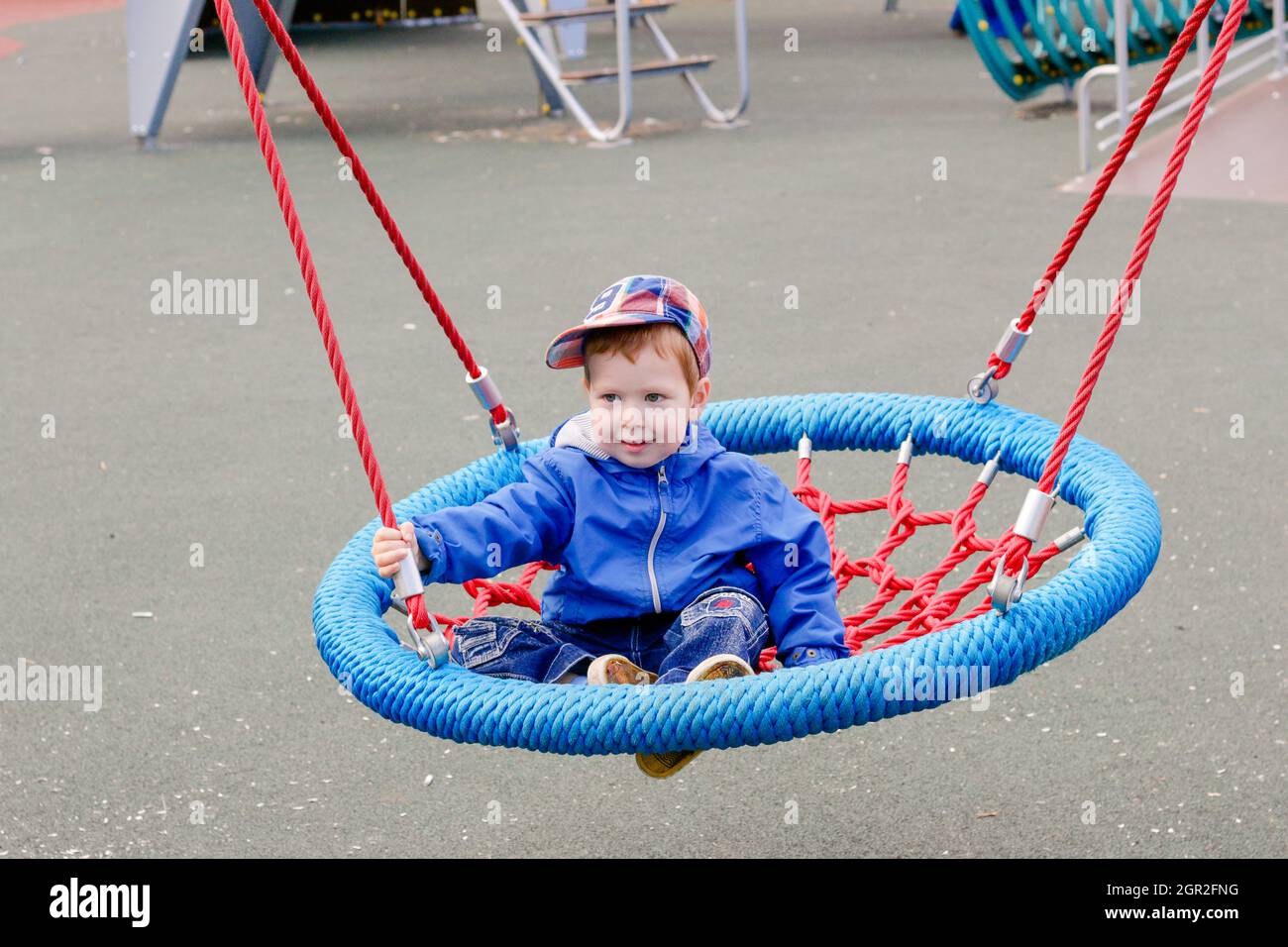 Niño paseos en un swing. Inusual Swing en el parque infantil. Entretenimiento durante el recreo. Los niños caminan Foto de stock