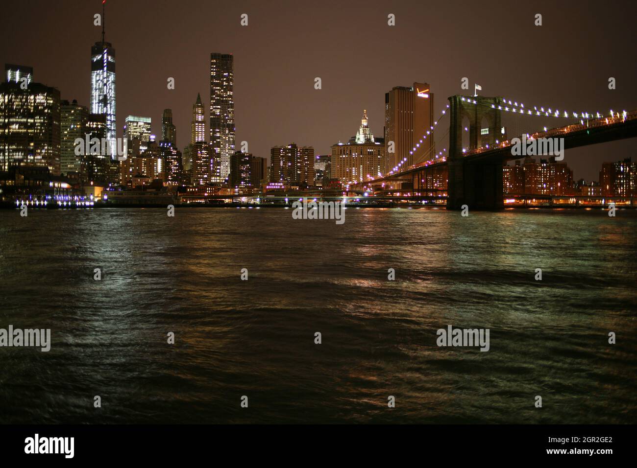 Puente sobre el rio iluminada por los edificios contra el cielo en la noche Foto de stock
