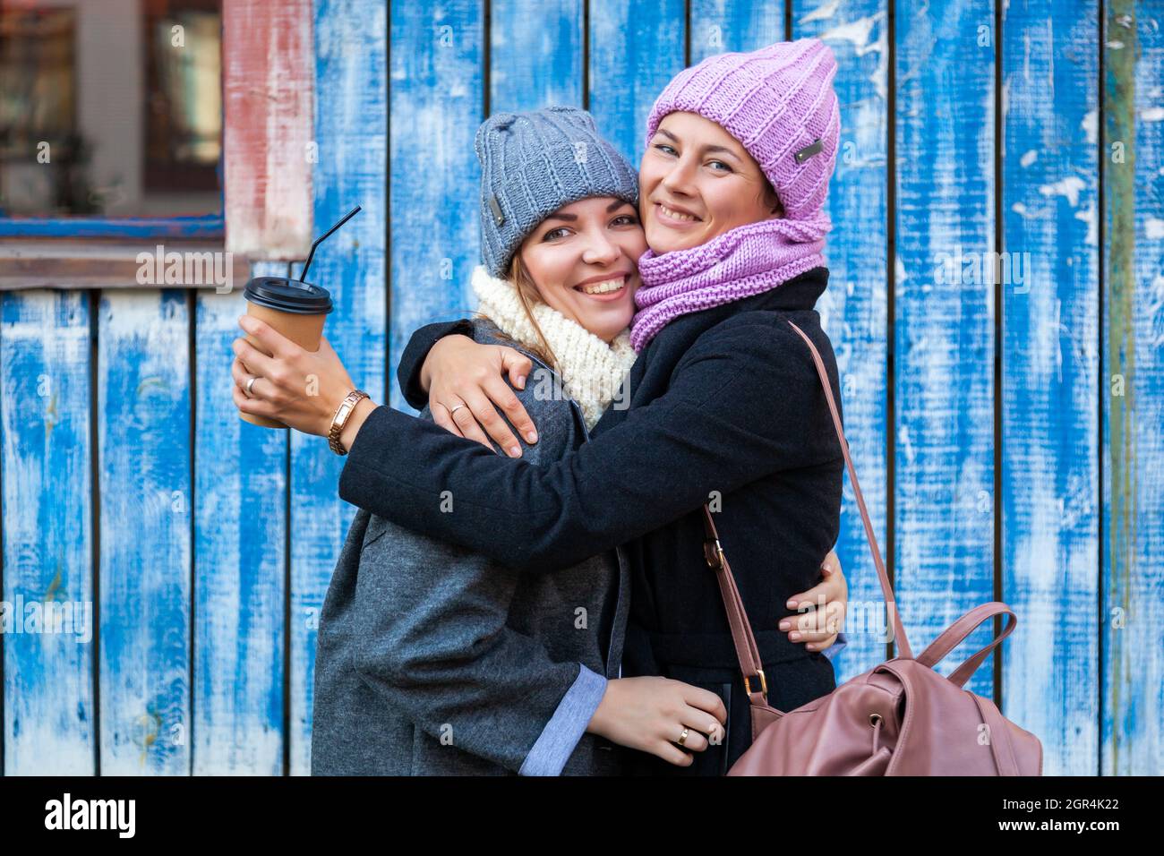 Una mujer joven Amigos en Un abrazo de ropa con estilo, charla y bebe café  para ir alrededor de la pared azul Fotografía de stock - Alamy