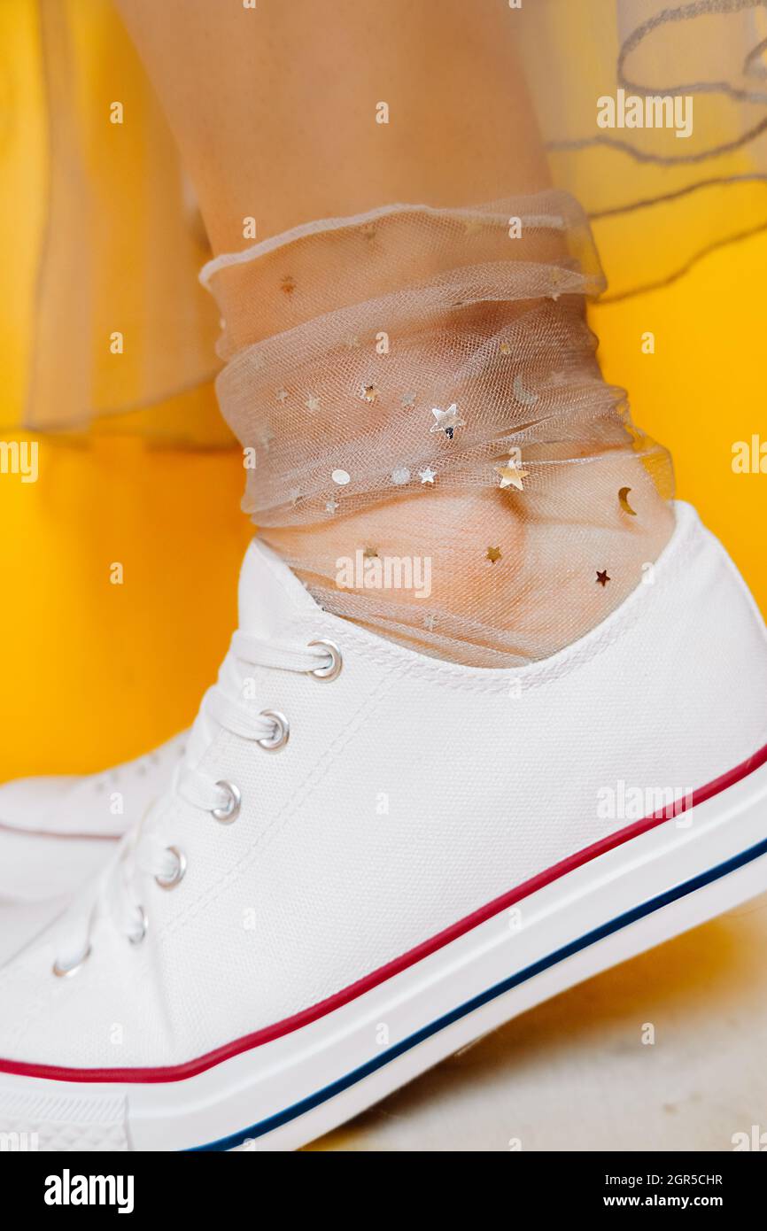 Piernas de mujer en White Sneakers, calcetines transparentes Silver Stars y vestido de tulle exuberante amarillo Fotografía de stock -