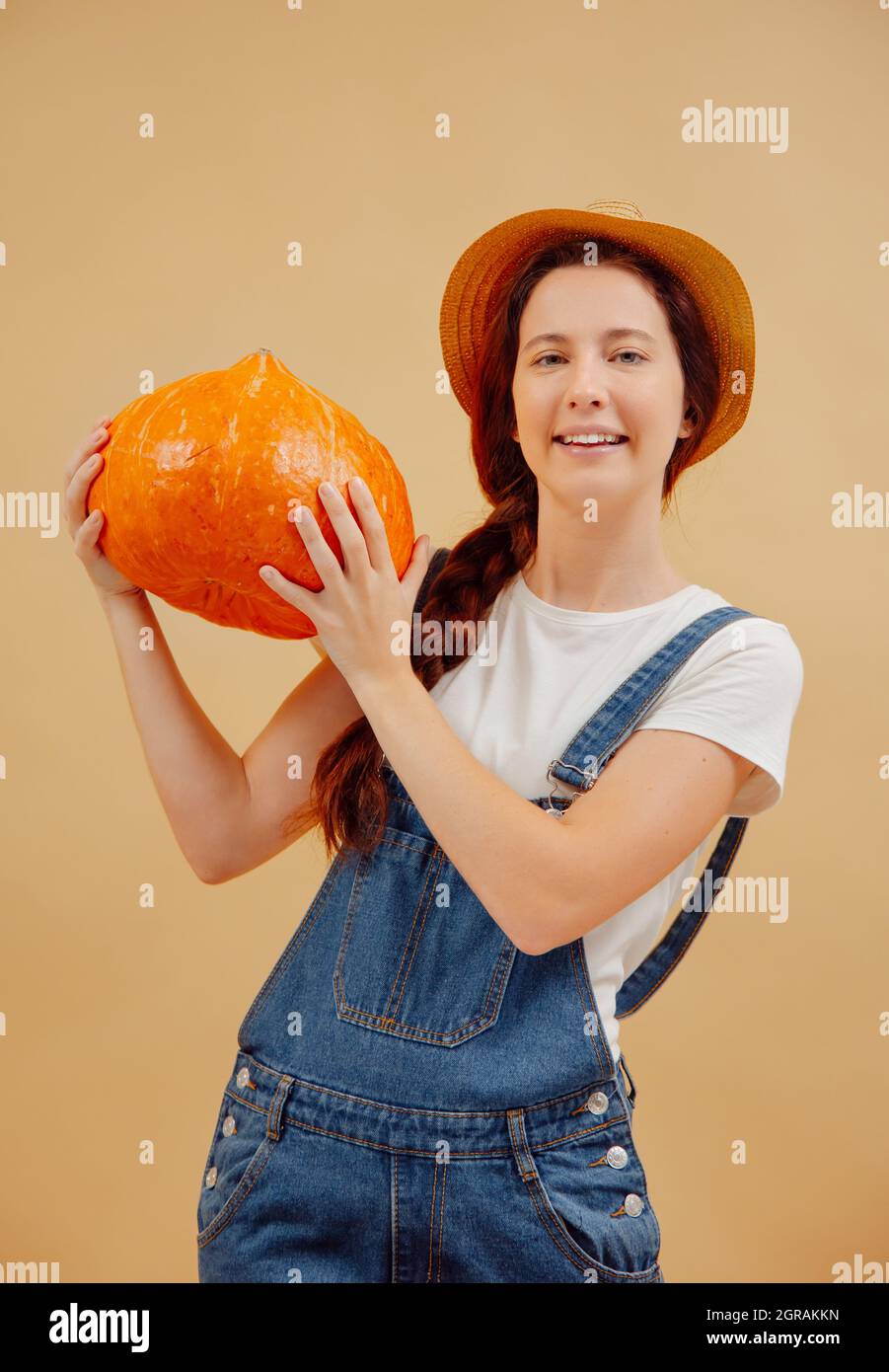 Jardinero mujer caucásica bastante alegre con sombrero y guantes de  jardinería sosteniendo maceta y mirando a pala aislado en la pared naranja  con espacio de copia
