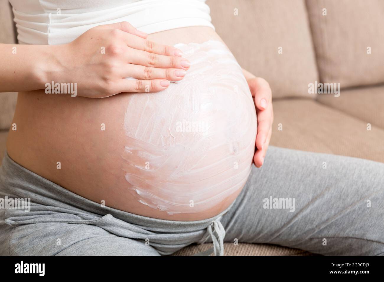 Una chica embarazada se sienta en casa en la cama y le da una crema  antiestiramiento Mark Cream en el estómago Fotografía de stock - Alamy
