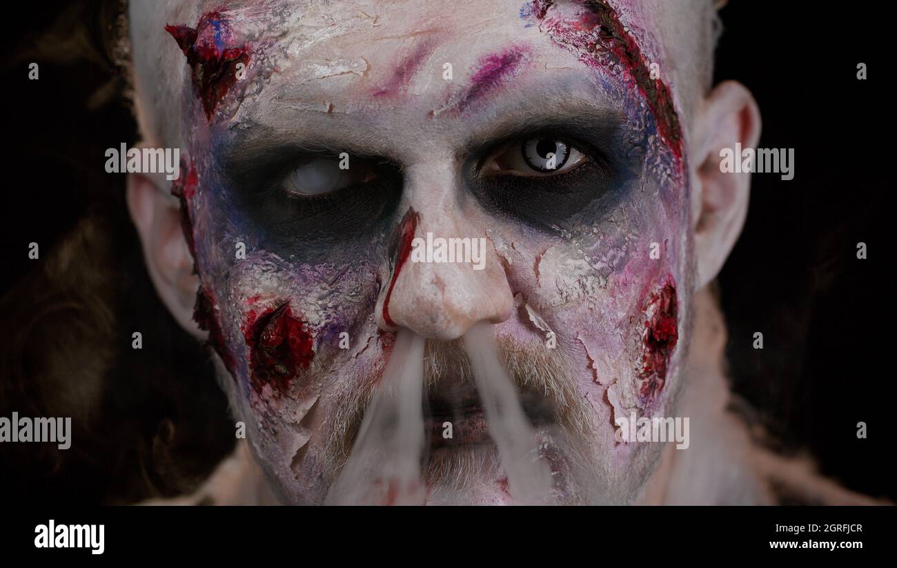 Hombre zombie con maquillaje con heridas cicatrices y lentes de contacto  blanco sopla humo de la boca, sonriendo Fotografía de stock - Alamy