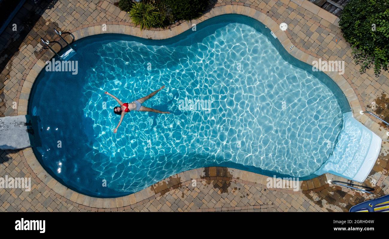 Vista aérea de una mujer flotando en una piscina el día de verano. Foto de stock