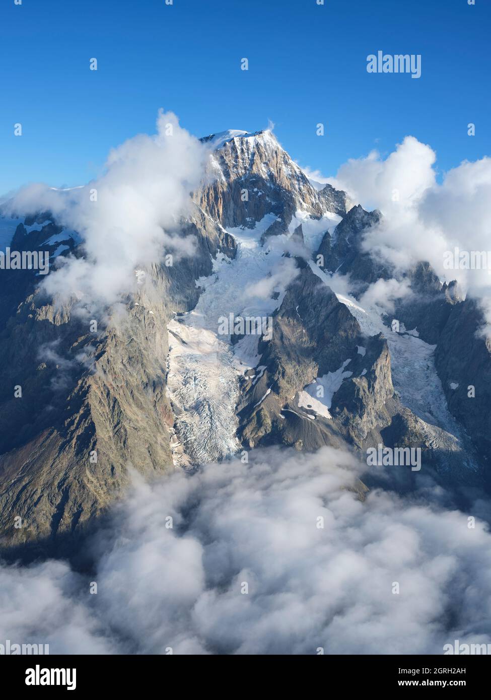VISTA AÉREA. Cara oriental del Mont Blanc en la luz de la mañana sobre algunas nubes bajas. Courmayeur, Valle de Aosta, Italia. Foto de stock