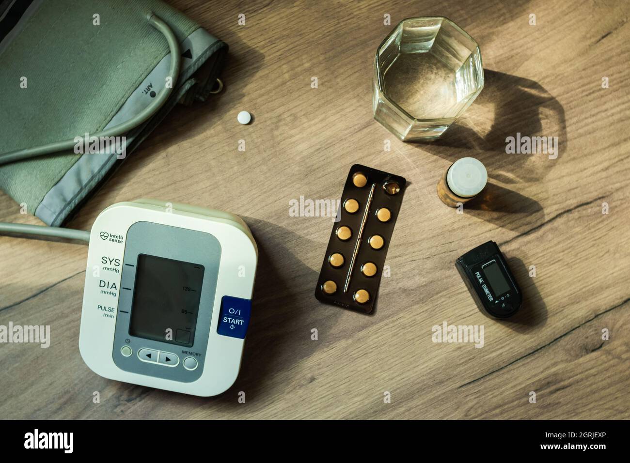En la mesa hay pastillas, un dispositivo de medición de la presión  arterial, un vaso de agua y un oxímetro. Un kit para personas mayores.  Vista superior. Concepto de salud Fotografía de