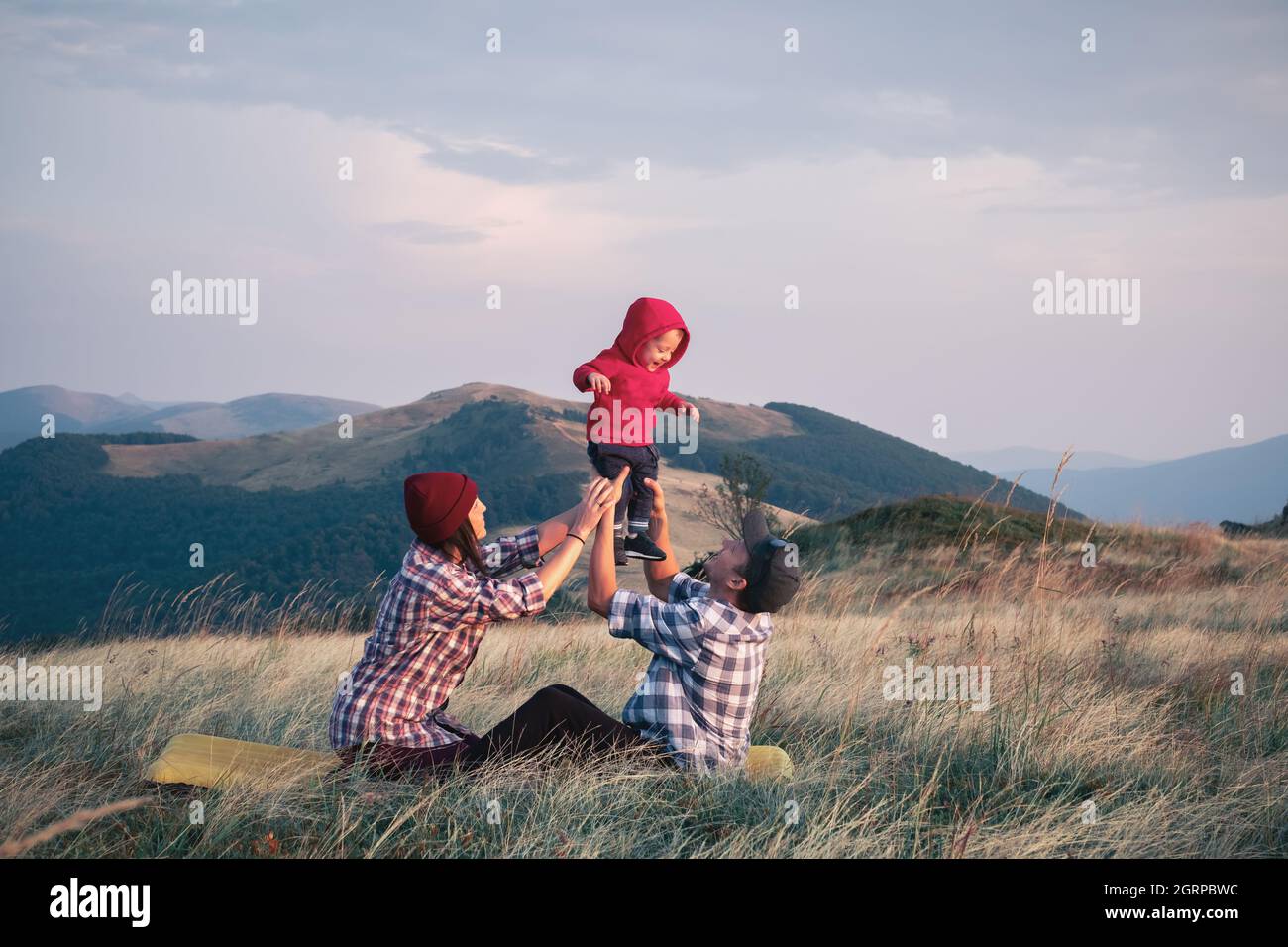 Padres con hijo en un prado de hierba en las montañas de otoño. Viaje con concepto de niño Foto de stock