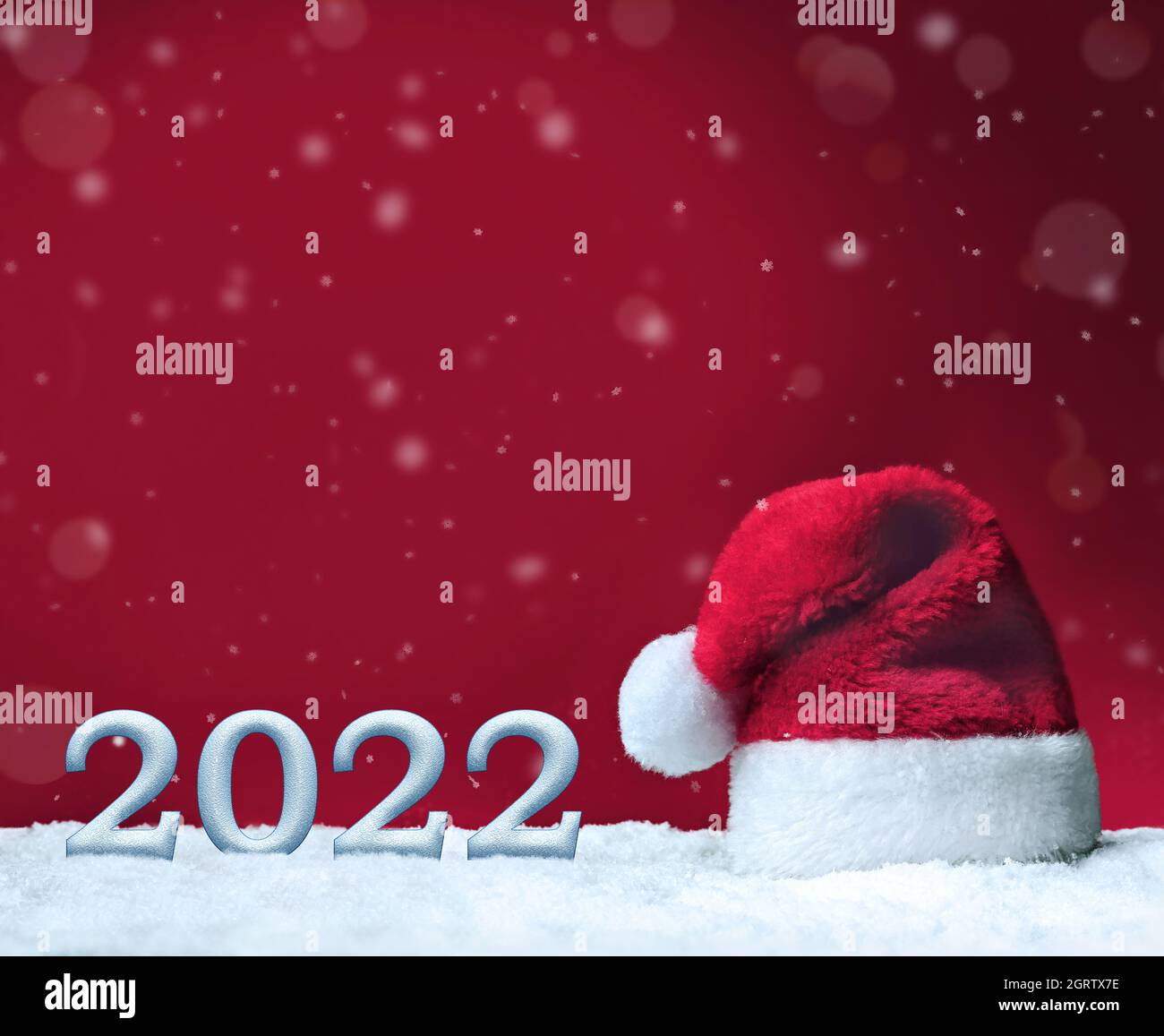 Sombrero de Santa en la nieve sobre fondo rojo, decoración de Navidad. Concepto de vacaciones. 2022. Foto de stock