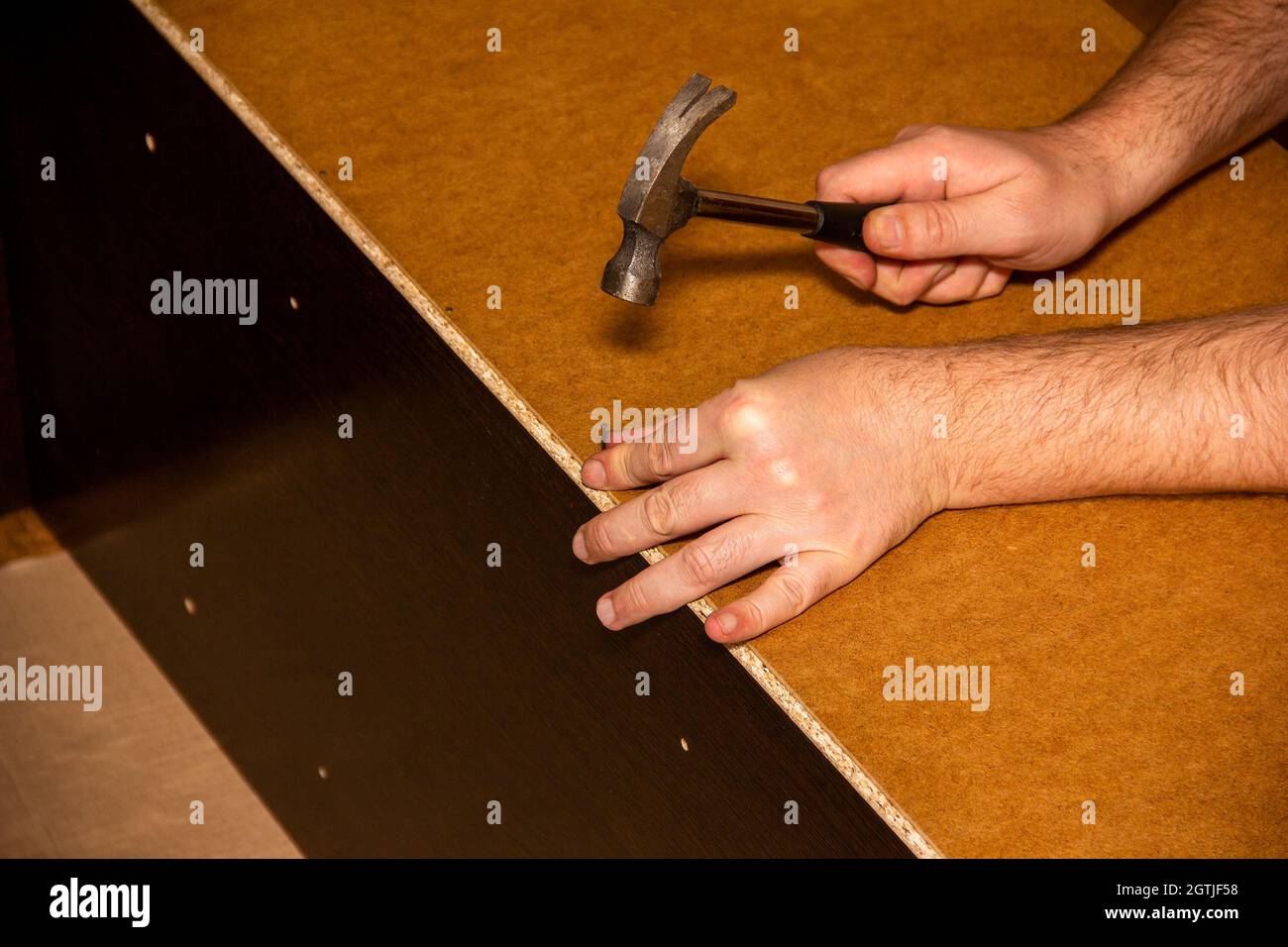 Un fabricante de muebles de carpintero golpea Una uña en la parte trasera  del gabinete con un martillo Fotografía de stock - Alamy