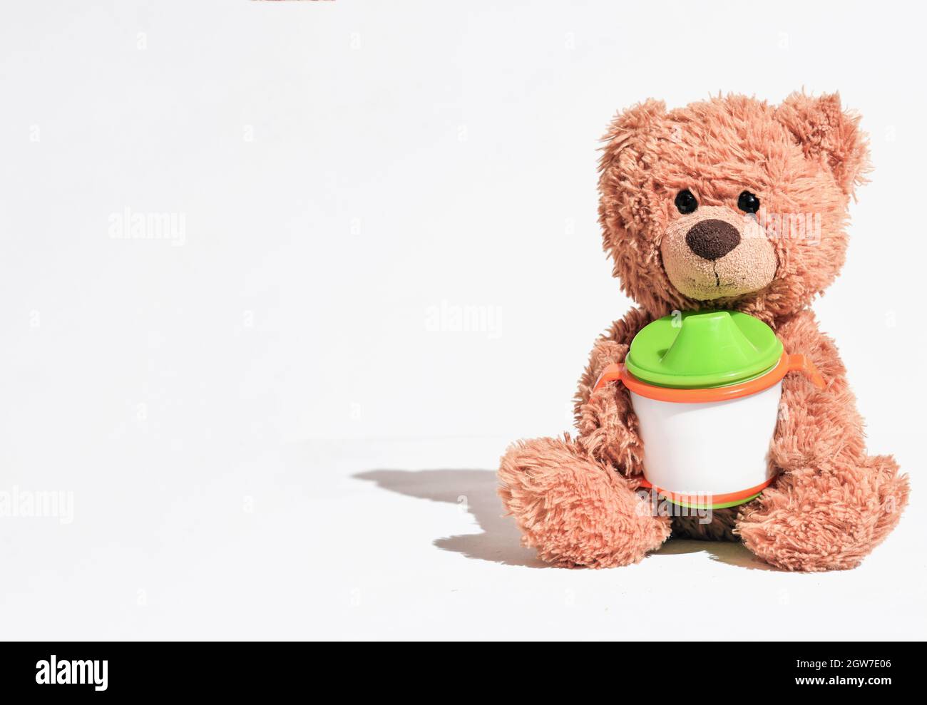 oso de peluche sentado sobre fondo blanco y sosteniendo el vaso del bebé.  concepto de la nutrición de los cabritos, primer alimento del bebé. espacio  de la copia para el texto Fotografía
