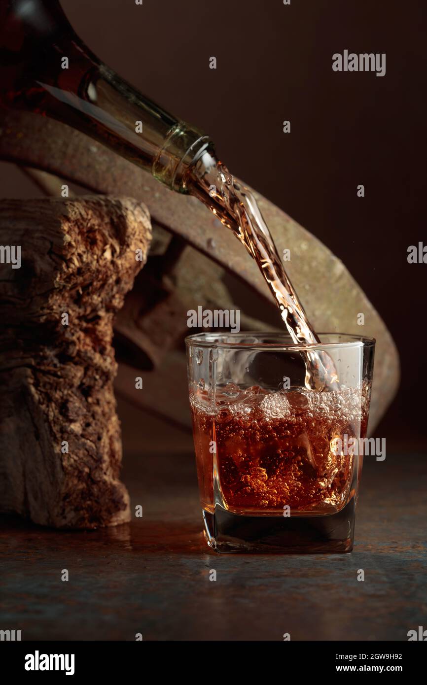 El whisky se vierte de una botella en un vaso congelado con hielo natural.  Fondo rugoso Fotografía de stock - Alamy